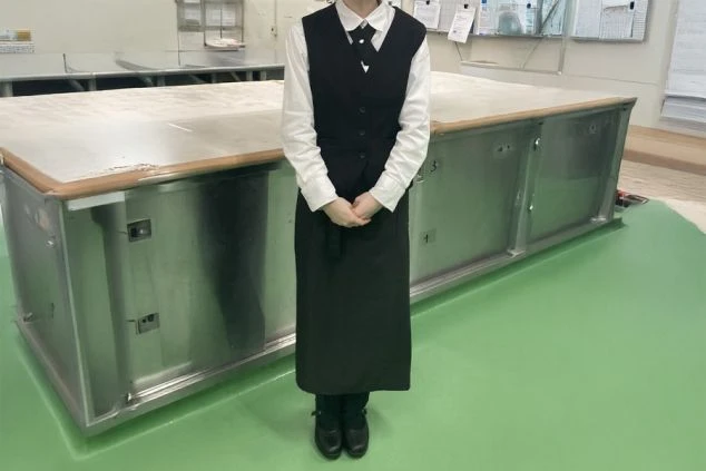 レストランで働く女性スタッフ。白いシャツに黒いベストとロングエプロンを着用。落ち着いた雰囲気の制服で、レストランサービスの仕事をイメージさせる。