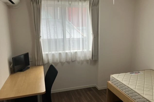 リゾートバイトの社員寮の部屋を表現するイメージ画像。ベッドと机、テレビが備え付けられたシンプルな個室。