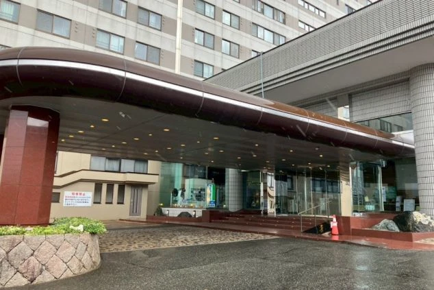 入口。モダンなデザインの庇と、ガラス張りの自動ドア、赤い大理石のような柱。