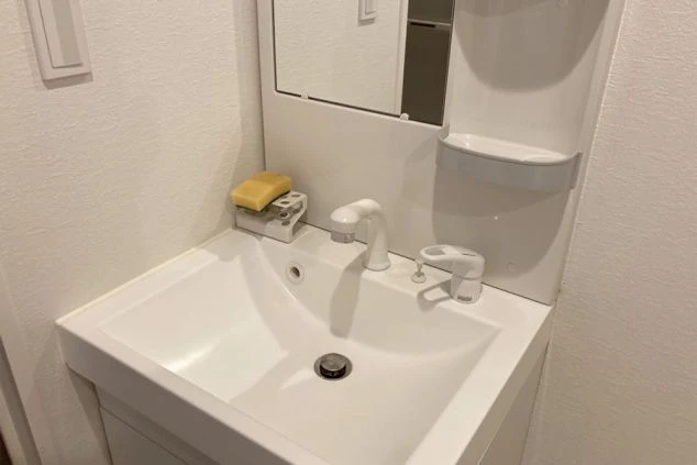 寮の洗面台。鏡と清潔な洗面ボウルが映る。