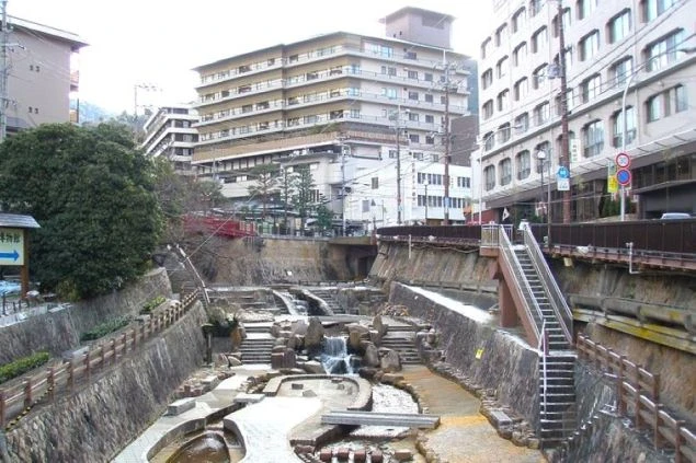温泉街の川沿いの風景。中央の石積みで整備された川底には湯が流れ、両側には石垣が続き、その上には大きな温泉旅館やホテルが立ち並んでいる。