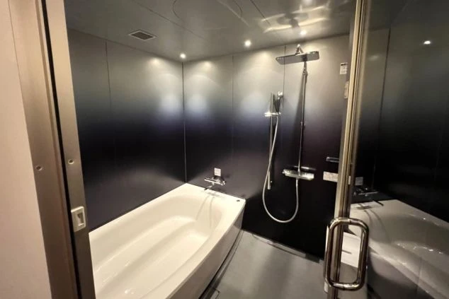 黒い壁に白い浴槽とシャワーが備え付けられた、モダンでシンプルな浴室