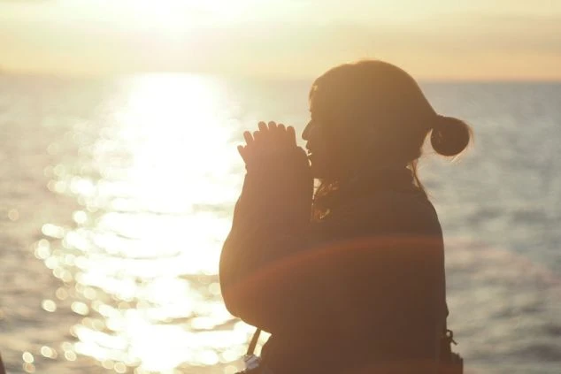 昇る朝日に照らされる女性のシルエット。リゾートバイトで、感動的な日の出とともに新しい一日を迎えませんか？