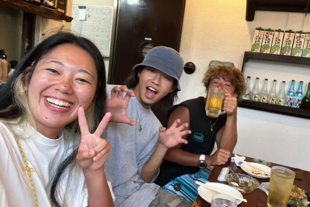  賑やかな居酒屋で楽しそうにポーズをとる友人たち。ビールジョッキを片手に、笑顔で乾杯している様子。