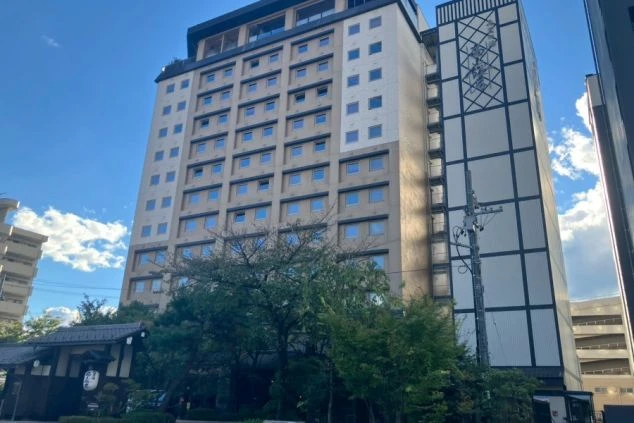 和風の低層の建物と、その奥にそびえるモダンな高層のホテルの全景。建物側面に「高山桜庵」の文字が見える。