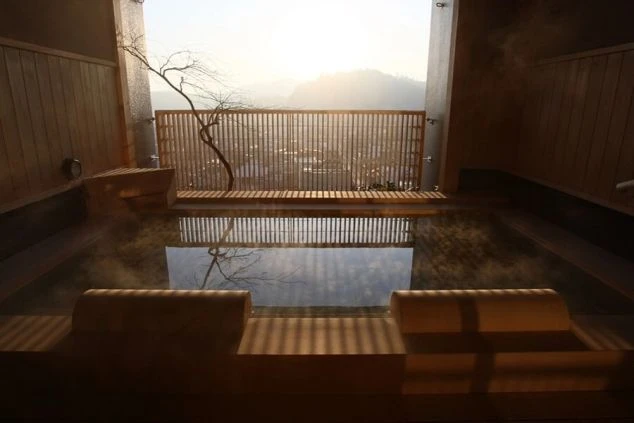 客室露天風呂。窓の外に飛騨高山の町並みと山々を望む、朝日が差し込む温泉。