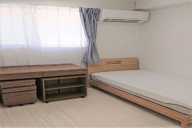 白い壁とベージュの床が柔らかい雰囲気の部屋に木製の茶色いベットフレームに白いマットレスが敷かれておりその横には木製のデスクが置いてありシンプルなデザインの部屋です