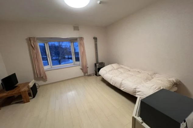 ワクトリの社員が出張で撮影した、リゾートバイトの寮の一室。シンプルなフローリングの部屋には、布団、ストーブ、テレビが備え付けられており、窓の外には雪景色が広がる。リゾートバイト中の生活環境を示す。
