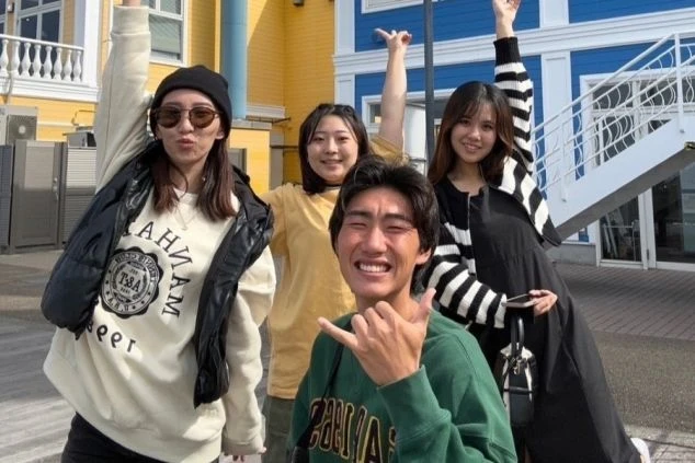 カラフルな建物を背景に、楽しそうにポーズをとる5人の友人。笑顔いっぱいで、仲の良さが伝わる集合写真。