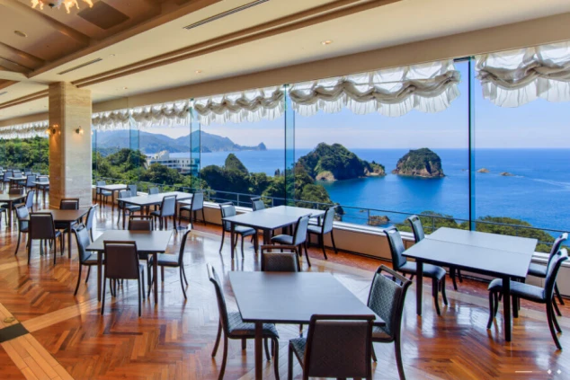堂ヶ島にあるホテルのレストランの画像。大きな窓からは雄大な海と奇岩、そして緑豊かな島々が見渡せる。洗練された空間で食事をしながら絶景を楽しめる、リゾートバイトの職場となる施設の雰囲気。