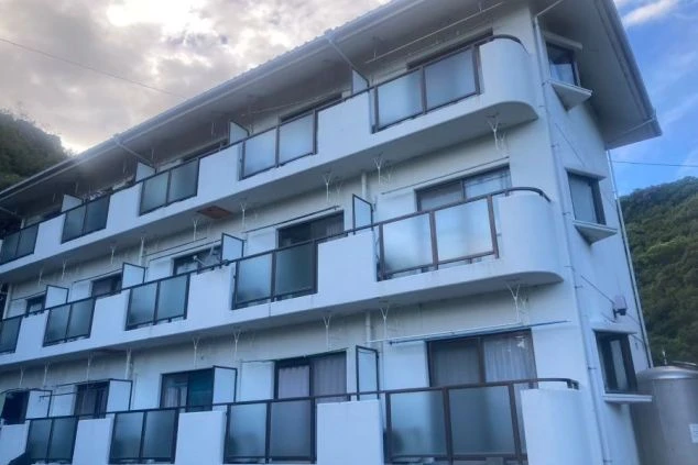 白い建物全体を捉えた画像。ベランダにはそれぞれ窓がついており、リゾートバイトの寮や社宅として利用されるアパートやマンションの画像。