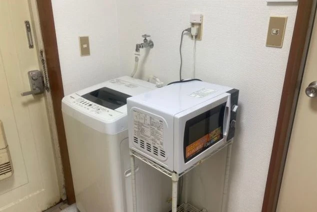 洗濯機と電子レンジが並べて置かれている画像。寮に備え付けられている家電で、リゾートバイト中の生活に役立つ。リゾートバイトの寮の共用スペースの画像。