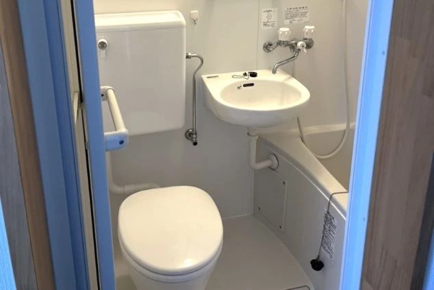 白を基調とした、清潔感のあるユニットバスの画像。便座、洗面台、バスタブがまとまって配置されている。リゾートバイトの寮の風呂場の画像。