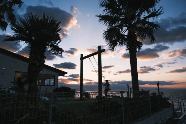 夕焼けの空の下、ヤシの木と海岸線がシルエットになっている。太陽が地平線に沈み、空をオレンジ色と紫色に染めている