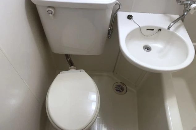 個室内のコンパクトなトイレと手洗いボウルの様子。白で統一された清潔感のある空間で、温水洗浄便座などは付いていないシンプルな造りのサニタリー設備。