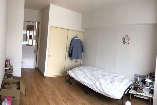 白を基調としたシンプルな寮の個室。フローリングの床にシングルベッドとクローゼットが配置され、壁には折り紙の飾りが貼られている。生活感のある落ち着いた雰囲気の居室。