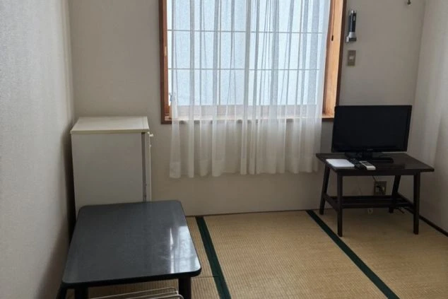 清潔な畳敷きの和室に、テレビ、小型冷蔵庫、ローテーブルが完備された個室寮の画像。