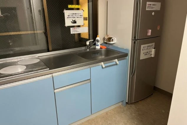 京都府嵐山のリゾートバイトの寮のキッチンの画像。IHの二口コンロと冷蔵庫完備で、引き出しの水色が印象的。