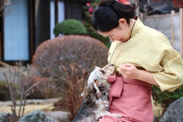 リゾートバイトの勤務先宿泊施設の庭で、仲居さんが可愛らしい犬と遊んでいる様子。仕事中のイメージ。