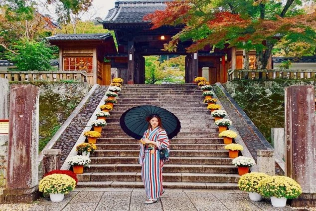 紅葉が美しい寺院の階段で和装の女性が和傘を差している写真。リゾートバイトを通して、仕事の合間や休日にこのような歴史ある観光地を訪れて旅気分を味わえる魅力を伝えます。