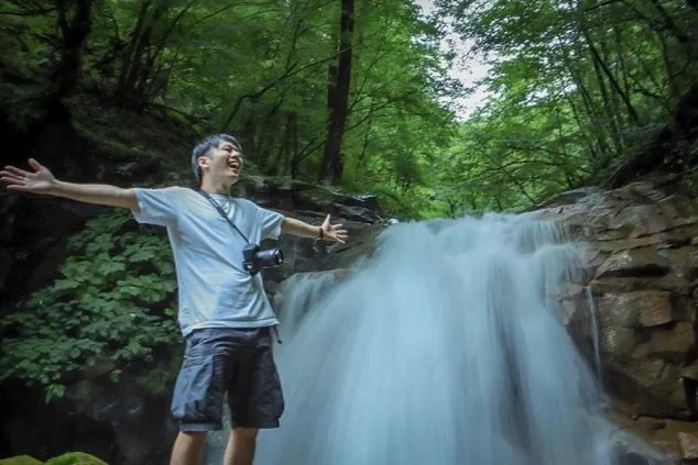 森の中の滝の前で両手を広げて喜ぶ男性。リゾートバイトの休日の過ごし方。自然アクティビティを楽しめる環境。