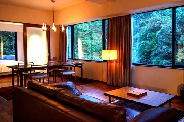 ホテルの豪華な客室。窓から緑豊かな森が見え、ソファやダイニングテーブルが並ぶ職場のイメージ画像。