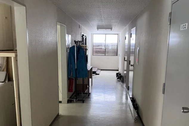 リゾートバイトの寮の廊下の画像。白い壁と床が続き、奥には窓があり、右側には部屋のドアが並んでいる。共同生活の場としての寮の内部。