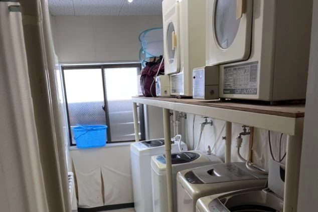 リゾートバイトの寮のランドリースペースの画像。複数の洗濯機と乾燥機が並び、窓からは明るい光が差し込む。リゾートバイト中の洗濯に便利な設備。