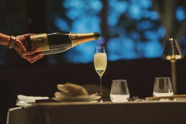 レストランでシャンパンをグラスに注ぐサービススタッフの手元が映るイメージ画像。リゾートバイトの職場の様子。