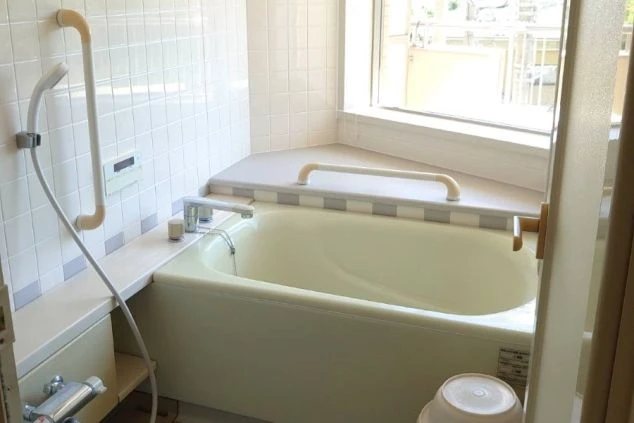 ワクトリの社員が出張で撮影した、リゾートバイトの客室寮のバスルームの画像。白いタイル張りの浴槽とシャワーが備え付けられており、窓からは明るい光が差し込む。手すりも設置され、安心して利用できる。