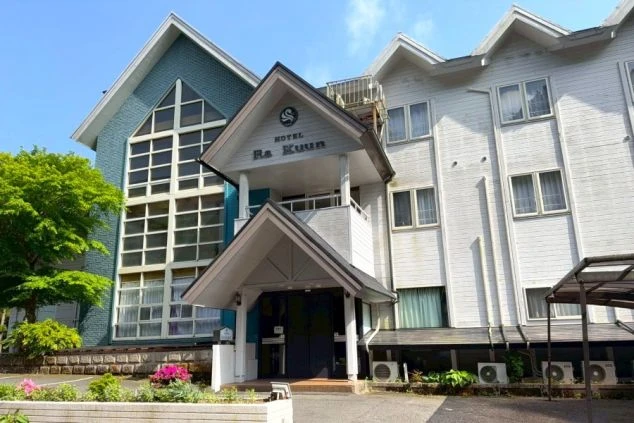 白と青のコントラストが特徴的な洋風のホテルの外観画像。緑豊かな季節のリゾートバイトの勤務地のイメージを伝える。