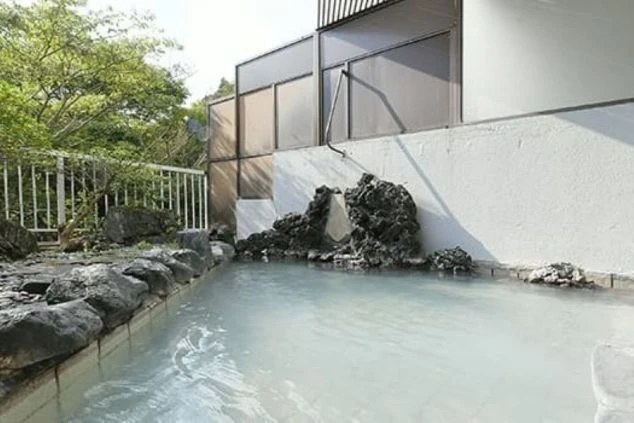 岩と白いタイルで作られた、自然の中に溶け込むような露天風呂の画像。青白い湯の色が特徴的で、温泉地でのリゾートバイトの魅力をアピール。