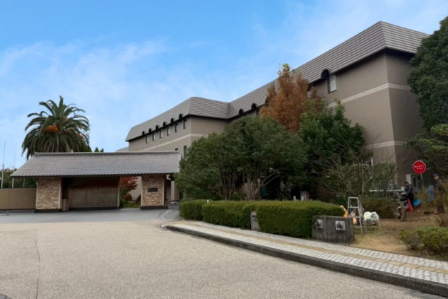 手前には和風の門構えがあり、周囲には豊かな木々が植えられています。