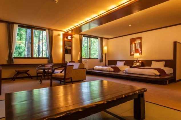 和室とベッドルームが一体となった広々とした客室の画像です。窓からは豊かな緑が見え、落ち着いた雰囲気の旅館やホテルの客室でのリゾートバイトのイメージが伝わります。