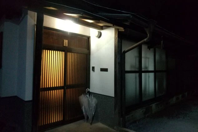 リゾートバイトの寮の外観。夜の風景で、温かみのある光が玄関を照らし、和風の引き戸が印象的。