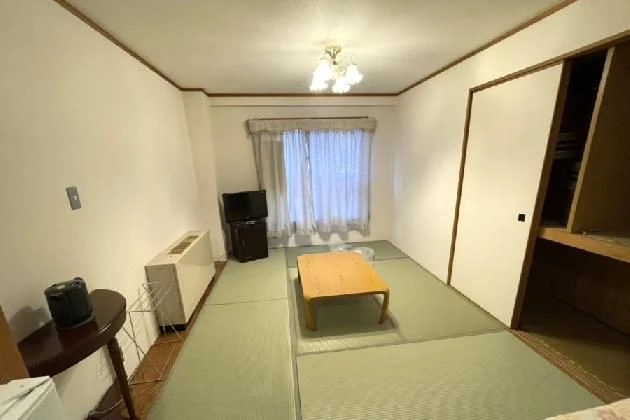 畳敷きの和室。中央にローテーブルがあり、奥の窓には白いカーテンがかかっている。