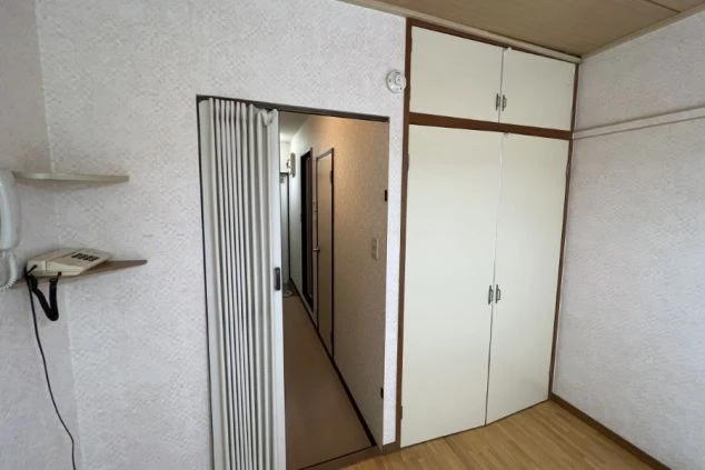 ワクトリの社員が出張で撮影した、リゾートバイトの寮の部屋の画像。白い壁にクローゼットと棚、電話が設置されており、奥には廊下が見える。生活感があり、収納スペースが確保された寮の様子。