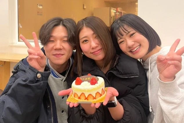 3人の若い男女が誕生日ケーキを持ってピースしている写真。リゾートバイトで出会った仲間と誕生日を祝う様子。