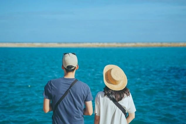 南国リゾートの青い海を眺める二人。リゾートバイトの休日の観光、絶景。