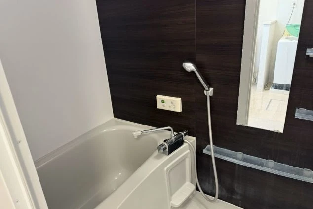 浴室。ダークブラウンの壁で、浴槽とシャワーが備え付けられている。