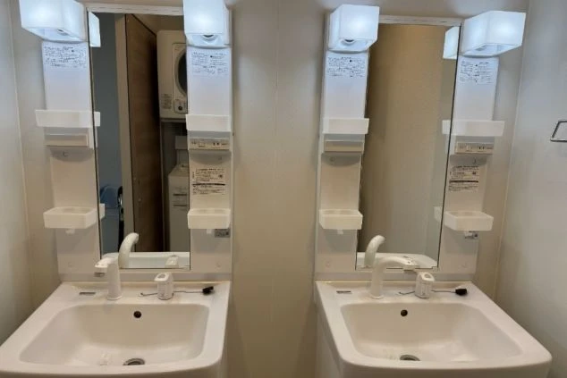 寮の洗面台。左右に鏡と照明付きの洗面台が並んでおり、奥に洗濯機が見える。