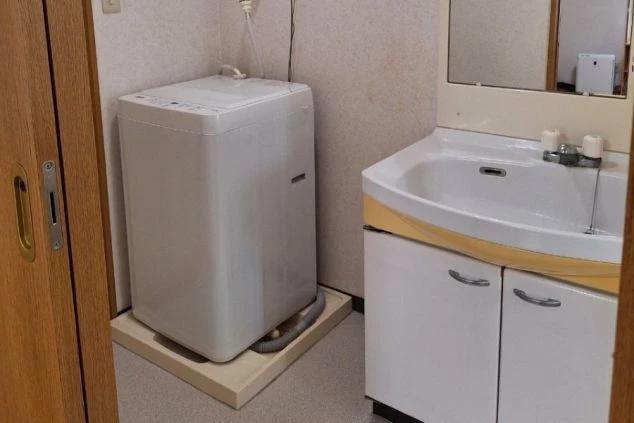 リゾートバイトの個室寮に完備された洗濯機と洗面台の画像。部屋の中に洗濯機があるため、共同スペースではなくプライベートな空間で洗濯ができることが伝わる画像。