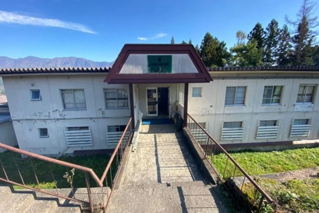 青空の下、山を背景に立つリゾートバイトの寮の外観。階段があり、落ち着いた雰囲気の中で生活できることが伝わる画像。