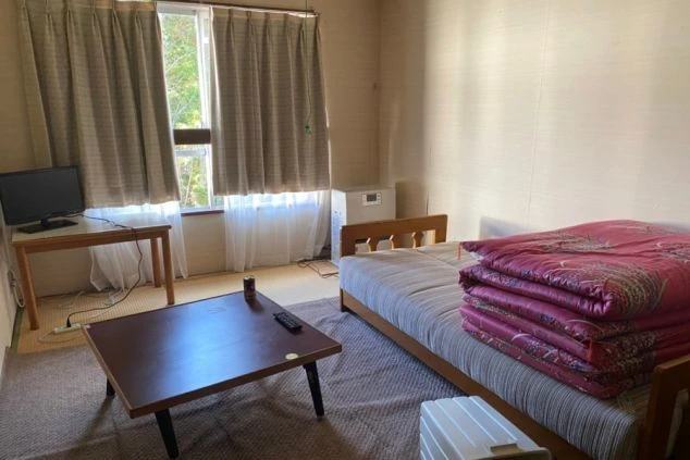 リゾートバイトの個室寮の室内。シングルベッド、テレビ、テーブル、ミニ冷蔵庫が備え付けられており、プライベートな空間でくつろげる設備の画像。