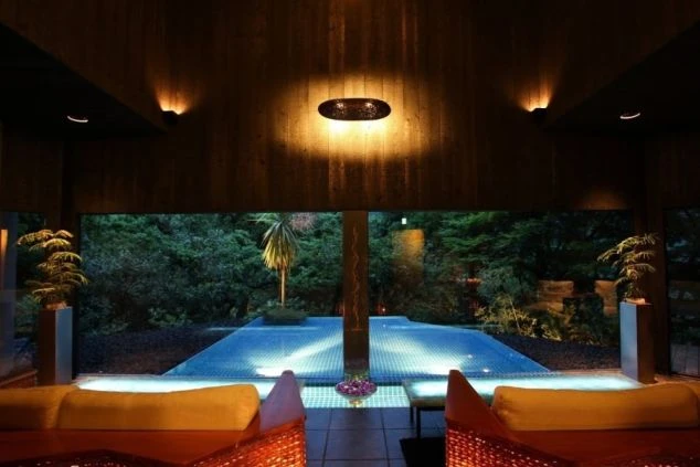 箱根吟遊のプールエリアの画像。落ち着いた照明とモダンな空間デザインで、大きな窓の向こうにはライトアップされた木々とプールが見える。