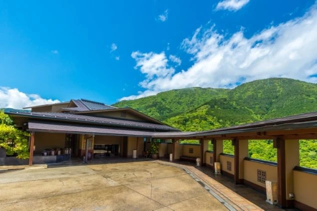 箱根吟遊の外観。緑豊かな山々を背景に、瓦屋根の落ち着いた和風建築が広がるの画像。広々としたエントランスと廊下が特徴的で、リゾートバイトの職場となる旅館の、自然に囲まれた美しい雰囲気を伝える。