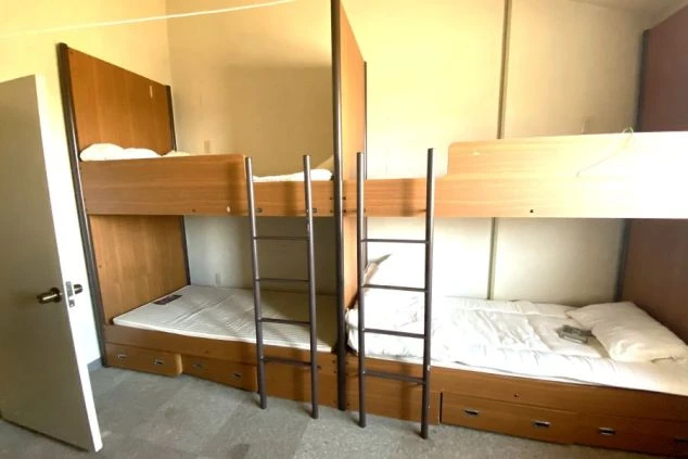 清潔なシーツと木目調の二段ベッドが用意されたリゾートバイトの寝室。