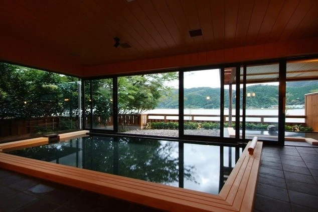 大きな窓から湖の絶景を望む、広々とした内風呂。ヒノキの縁取りが施された湯船に浸かりながら、開放的な景色を楽しめる贅沢な空間。