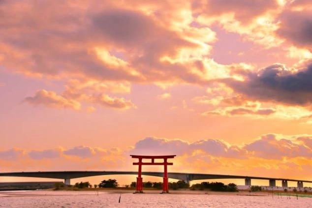 夕暮れ時の浜名湖に立つ弁天島海浜公園の赤い鳥居。背景には浜名湖を横断する浜名バイパスの大きな橋が見え、空全体がオレンジ色からピンク色に染まるドラマチックな夕焼け雲に覆われています。