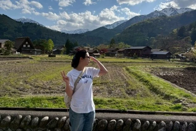 岐阜県白川郷の田んぼと合掌造りの家々を背景に山を望む女性。